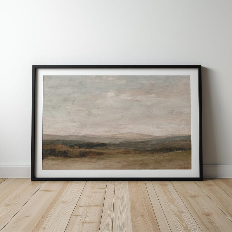 May include: A framed landscape painting with a black frame. The artwork depicts a serene scene of rolling hills and a cloudy sky, with muted tones of green, brown, and gray. The painting is displayed on a light wood floor.