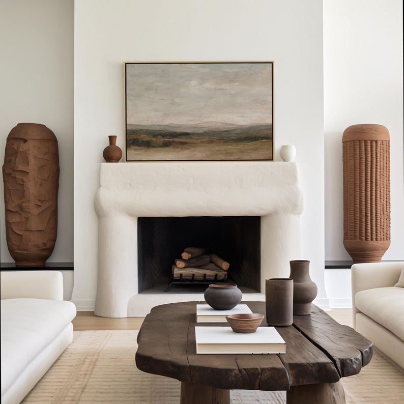 May include: A living room with a white fireplace, a landscape painting, and a dark wood coffee table. Two large, textured brown vases flank the fireplace. The coffee table displays books and decorative pottery.