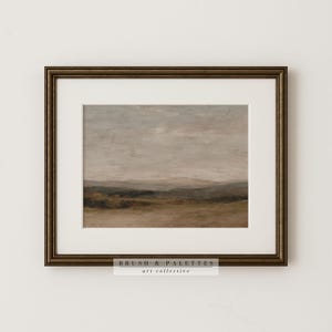 May include: Framed landscape art print featuring a muted color palette of browns, greens, and grays. The artwork depicts a serene countryside scene with rolling hills and a cloudy sky. The frame is a dark bronze color, and the print includes the text "BRUSH & PALETTES art collective."