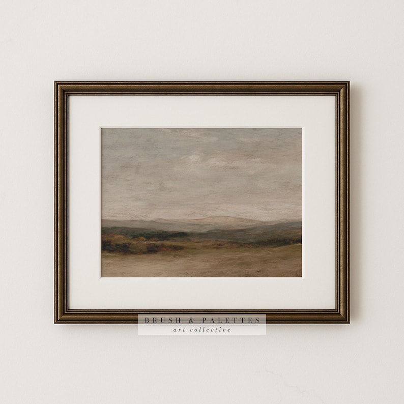 May include: Framed landscape art print featuring a muted color palette of browns, greens, and grays. The artwork depicts a serene countryside scene with rolling hills and a cloudy sky. The frame is a dark bronze color, and the print includes the text "BRUSH & PALETTES art collective."