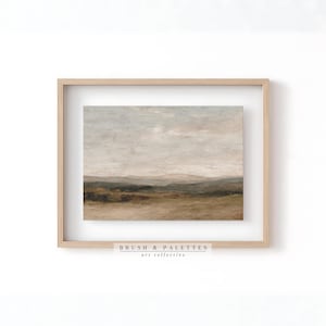May include: Framed landscape art print featuring a muted color palette of beige, brown, and gray. The artwork depicts a serene countryside scene with rolling hills and a cloudy sky. The frame is a light wood color. The text "BRUSH & PALETTES art collective" is at the bottom.