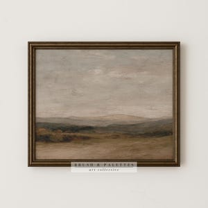 May include: A framed landscape painting with a muted color palette. The artwork depicts rolling hills and a cloudy sky, with shades of brown, green, and gray. The frame is a dark, ornate gold color. The text "BRUSH & PALETTES art collective" is at the bottom.