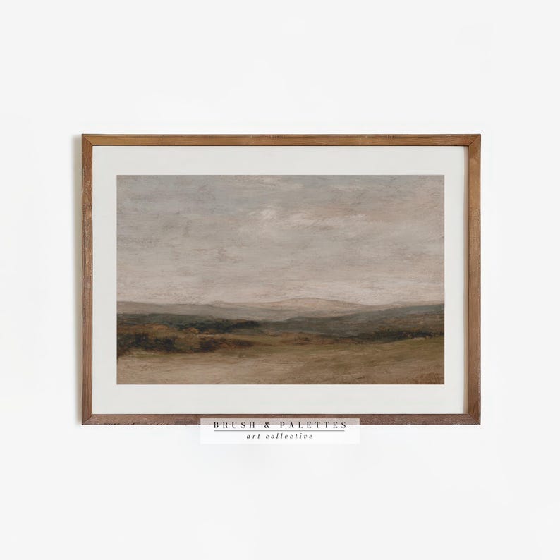 May include: A framed landscape art print featuring a muted color palette of beige, brown, and gray. The artwork depicts a serene countryside scene with rolling hills and a cloudy sky. The frame is made of wood. The text "BRUSH & PALETTES art collective" is at the bottom.
