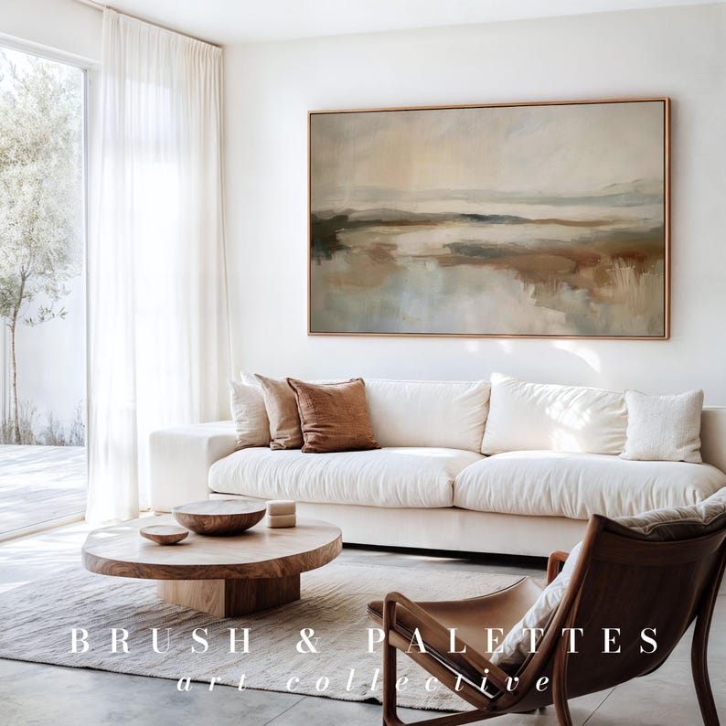 May include: A living room scene featuring a large abstract landscape painting in neutral tones above a white sofa with brown accent pillows. A wooden coffee table and a leather chair complete the decor. The text "BRUSH & PALETTES art collective" is at the bottom.