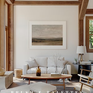 May include: A bright, airy living room with a neutral color palette. A framed landscape painting hangs above a white sofa. A wooden coffee table holds a vase and decorative items. The text "BRUSH & PALETTES art collective" is at the bottom.