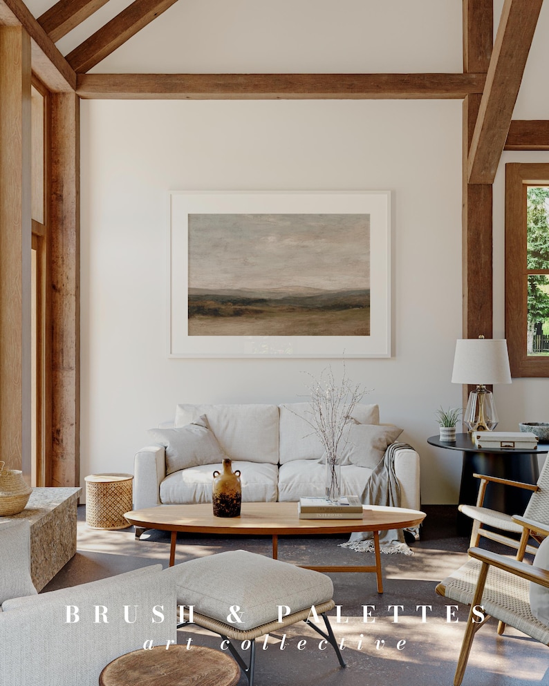 May include: A bright, airy living room with a neutral color palette. A framed landscape painting hangs above a white sofa. A wooden coffee table holds a vase and decorative items. The text "BRUSH & PALETTES art collective" is at the bottom.