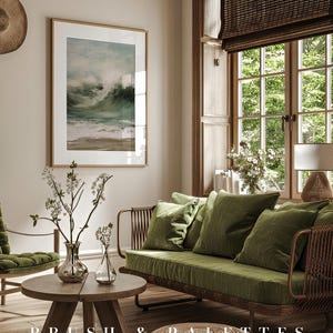 K&ouml;nnte beinhalten: Ein Wohnzimmer-Interieur mit einem gr&uuml;nen Samtsofa, einem Holz-Couchtisch und einem gerahmten Druck eines Meeresbildes. Das Sofa hat einen geflochtenen Rattanrahmen und ist mit Kissen dekoriert. Der Couchtisch ist rund und hat eine nat&uuml;rliche Holzoptik. Der Druck ist in einem hellen Holzrahmen und zeigt ein st&uuml;rmisches Meer mit Wellen, die an die K&uuml;ste krachen. Der Raum hat eine helle und luftige Atmosph&auml;re mit nat&uuml;rlichem Licht, das durch ein gro&szlig;es Fenster str&ouml;mt. Der Text "BRUSH & PALETTES art collective" ist auf dem Boden sichtbar.