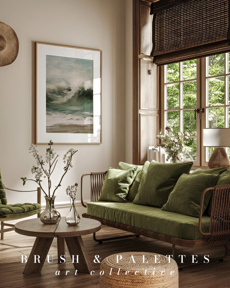 K&ouml;nnte beinhalten: Ein Wohnzimmer-Interieur mit einem gr&uuml;nen Samtsofa, einem Holz-Couchtisch und einem gerahmten Druck eines Meeresbildes. Das Sofa hat einen geflochtenen Rattanrahmen und ist mit Kissen dekoriert. Der Couchtisch ist rund und hat eine nat&uuml;rliche Holzoptik. Der Druck ist in einem hellen Holzrahmen und zeigt ein st&uuml;rmisches Meer mit Wellen, die an die K&uuml;ste krachen. Der Raum hat eine helle und luftige Atmosph&auml;re mit nat&uuml;rlichem Licht, das durch ein gro&szlig;es Fenster str&ouml;mt. Der Text "BRUSH & PALETTES art collective" ist auf dem Boden sichtbar.