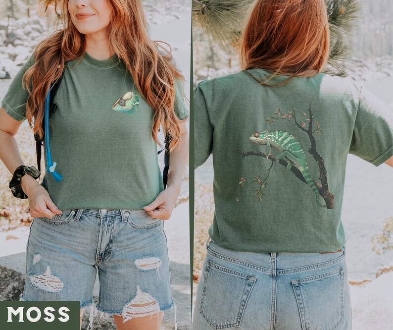 May include: A green t-shirt with a chameleon graphic on the back and a small graphic on the front. The t-shirt is being worn by a person with long red hair. The person is wearing blue denim shorts.