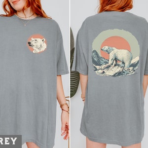 May include: A grey t-shirt with a graphic of a polar bear standing on a rock in front of a sunset. The graphic is on the back of the shirt.
