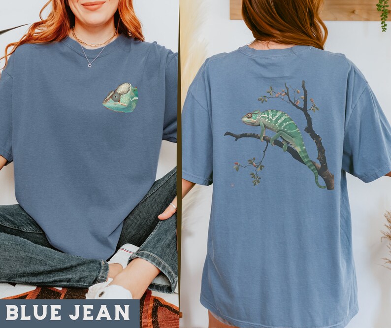 May include: A blue jean t-shirt with a chameleon graphic on the front and a larger chameleon graphic on the back. The chameleon on the back is on a branch with leaves and berries.
