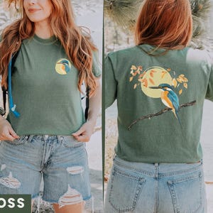 Puede incluir: Una camiseta verde con un gr&aacute;fico de p&aacute;jaro azul en la parte delantera y un gr&aacute;fico de p&aacute;jaro azul m&aacute;s grande en la parte posterior. La camiseta tiene un aspecto desgastado y est&aacute; hecha de una tela suave y c&oacute;moda.