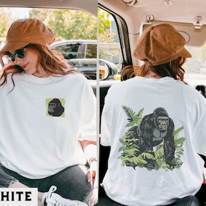May include: Two white t-shirts with a gorilla graphic print. One shirt features a small gorilla head print on the left chest, while the other shirt features a larger gorilla print with foliage on the back.