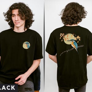 Puede incluir: Camiseta negra con un gr&aacute;fico de un p&aacute;jaro azul y verde en una rama con una luna amarilla en el fondo. El p&aacute;jaro est&aacute; posado en una rama con hojas. La camiseta tiene cuello redondo y mangas cortas.