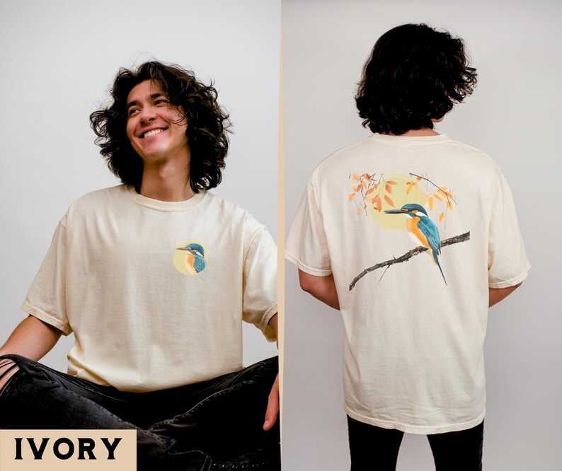 Puede incluir: Una camiseta de color crema con un gr&aacute;fico de un p&aacute;jaro azul y verde en la parte delantera y una versi&oacute;n m&aacute;s grande del mismo gr&aacute;fico de p&aacute;jaro en la parte posterior. El texto "IVORY" est&aacute; impreso en la parte inferior de la imagen.