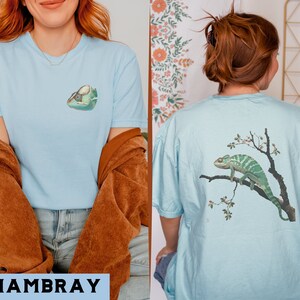 May include: Two light blue t-shirts with different chameleon designs. One shirt features a chameleon on a branch with pink flowers. The other shirt features a chameleon with its mouth open.