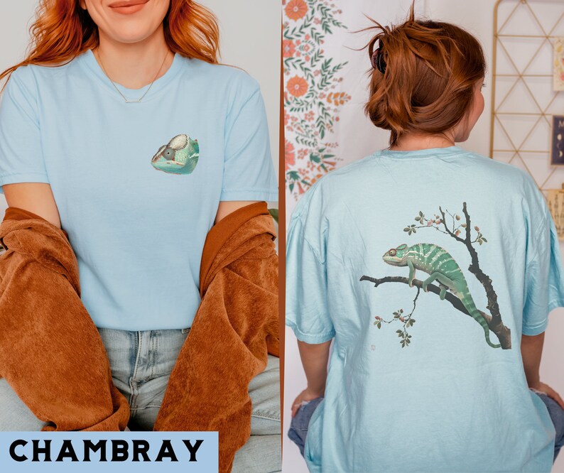 May include: Two light blue t-shirts with different chameleon designs. One shirt features a chameleon on a branch with pink flowers. The other shirt features a chameleon with its mouth open.