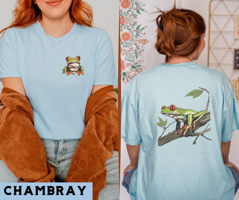 May include: A light blue t-shirt with a green tree frog on the front and a larger green tree frog on the back. The frog on the back is sitting on a branch with leaves.
