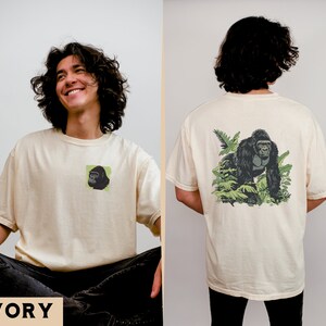 May include: A cream colored t-shirt with a black and green gorilla graphic on the back and a smaller version of the graphic on the front. The text "IVORY" is printed in black at the bottom of the image.
