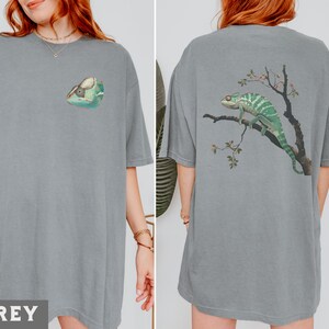 May include: Two grey t-shirts with a chameleon graphic. One shirt features a chameleon on a branch with flowers, the other shirt features a chameleon head.