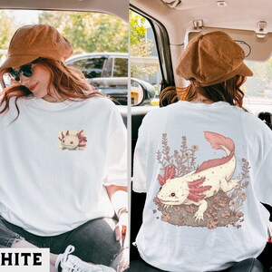 May include: White t-shirt with a pink and white axolotl illustration on the front and a larger pink and white axolotl illustration on the back. The axolotl is surrounded by small pink flowers.