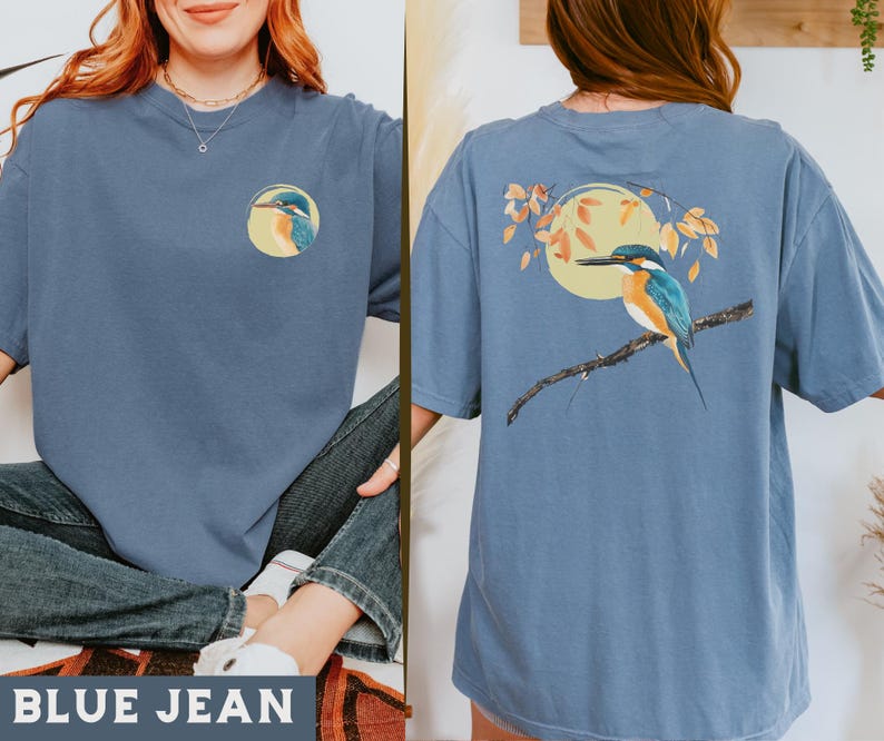 Puede incluir: Una camiseta azul jean con un gr&aacute;fico de p&aacute;jaro en la parte delantera y un gr&aacute;fico de p&aacute;jaro en la parte posterior. El p&aacute;jaro es un mart&iacute;n pescador con plumas azules, verdes y naranjas. La camiseta tiene un corte holgado y cuello redondo.