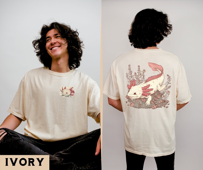 May include: A cream colored t-shirt with a small axolotl graphic on the front and a larger axolotl graphic on the back. The axolotl is pink and white with black eyes and is surrounded by pink flowers. The text "IVORY" is printed in black at the bottom of the image.