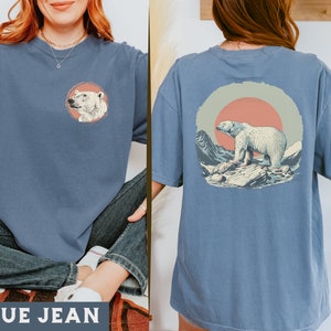 May include: A blue jean t-shirt with a polar bear graphic on the front and a polar bear graphic with a sunset in the background on the back. The shirt is made of a soft, comfortable material.