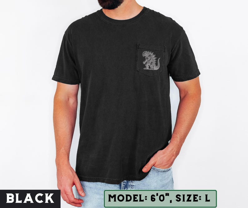 May include: Black t-shirt with a pocket featuring a detailed graphic of a monster. The shirt is a solid black color. The text "BLACK" is at the bottom left of the image. The text "MODEL: 6'0", SIZE: L" is at the bottom right.