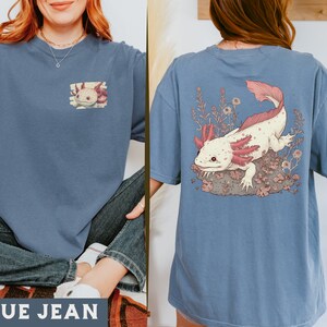May include: A blue jean t-shirt with a pink and white axolotl illustration on the back and a smaller version of the illustration on the front. The text "BLUE JEAN" is printed on the bottom of the image.