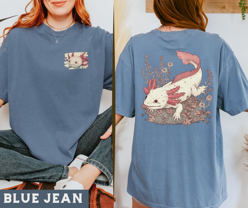May include: A blue jean t-shirt with a pink and white axolotl illustration on the back and a smaller version of the illustration on the front. The text "BLUE JEAN" is printed on the bottom of the image.