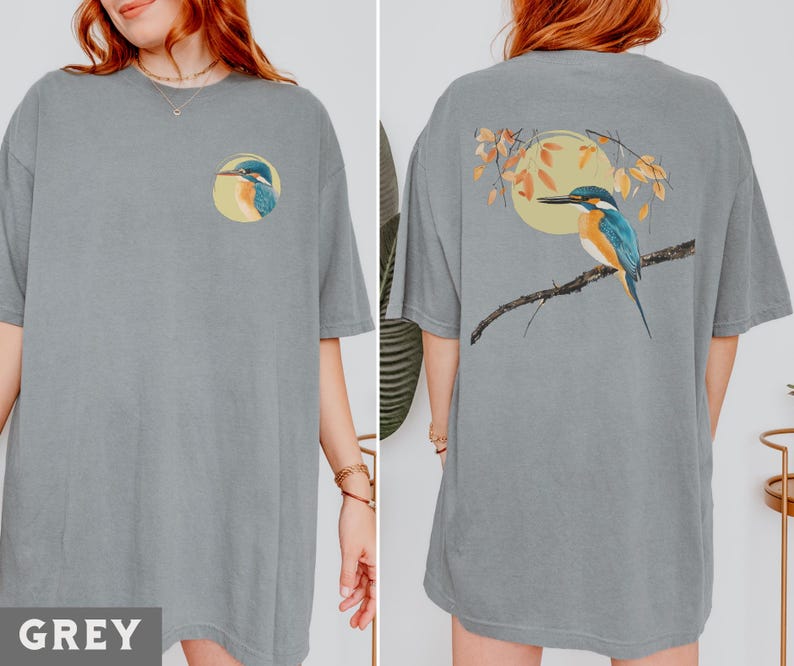 Puede incluir: Una camiseta gris de gran tama&ntilde;o con un gr&aacute;fico de un p&aacute;jaro en la parte delantera y un gr&aacute;fico de un p&aacute;jaro en la parte trasera. El gr&aacute;fico del p&aacute;jaro en la parte delantera es un primer plano de la cabeza del p&aacute;jaro. El gr&aacute;fico del p&aacute;jaro en la parte trasera muestra al p&aacute;jaro posado en una rama con hojas.