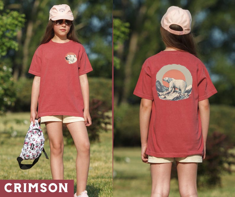 May include: A red t-shirt with a white polar bear graphic on the front and a white polar bear graphic on the back. The shirt has a crew neck and short sleeves. The polar bear graphic on the back is surrounded by a circle with a red sun and blue mountains.