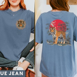 Op de afbeelding: Een jeansblauw T-shirt met een tijgerprint aan de voorkant en een tijgerprint met een rode zon en bamboe aan de achterkant.