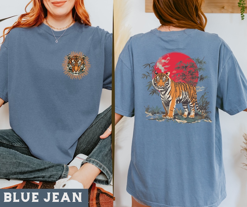 Op de afbeelding: Een jeansblauw T-shirt met een tijgerprint aan de voorkant en een tijgerprint met een rode zon en bamboe aan de achterkant.
