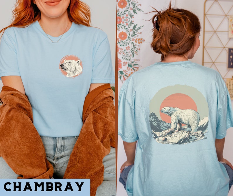 May include: Two light blue t-shirts with a polar bear graphic. One shirt features a polar bear head in a circle, the other features a polar bear walking in a landscape with a sunset.