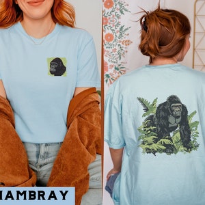 May include: Two light blue t-shirts with a gorilla graphic print. The first shirt features a close-up of a gorilla's face. The second shirt features a gorilla walking through a jungle scene.