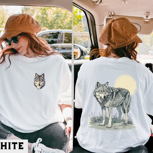 May include: Two white t-shirts with wolf graphic designs. One shirt features a wolf's head, the other a wolf howling at the moon.