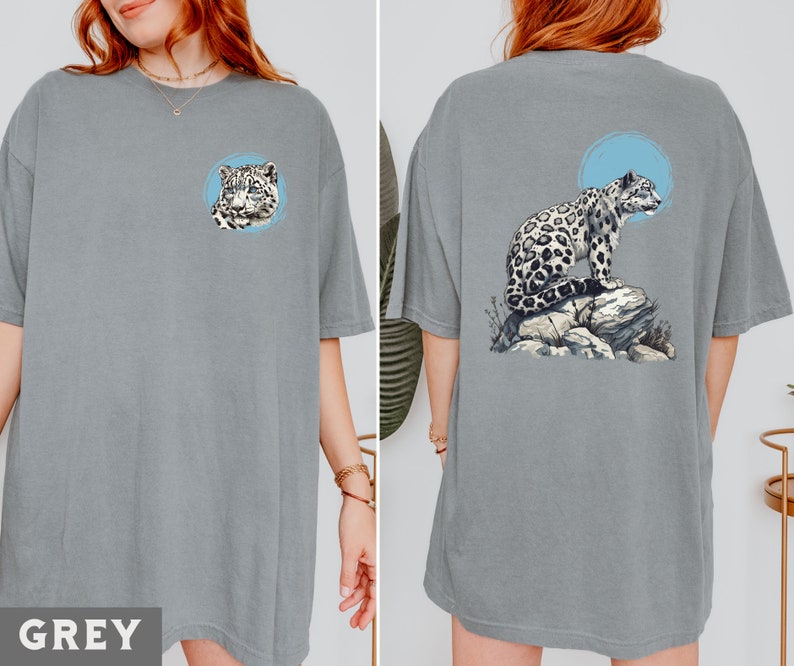 May include: A grey t-shirt featuring a graphic of a snow leopard sitting on a rock. The snow leopard is white with black spots and is looking to the right. The graphic is on the back of the shirt.