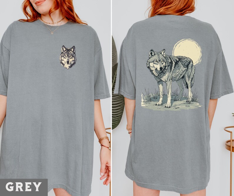 May include: Two grey t-shirts with a wolf graphic. One shirt features a wolf head graphic, while the other shirt features a wolf howling at the moon.