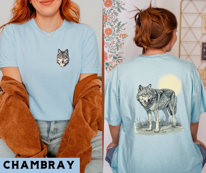 May include: Two light blue t-shirts with a wolf graphic. The shirt on the left has a wolf's head graphic, while the shirt on the right has a wolf howling at the moon graphic. The word "CHAMBRAY" is printed in black at the bottom of the image.