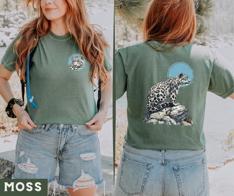 May include: A green t-shirt featuring a snow leopard graphic on the back and a snow leopard head on the front. The shirt is being modelled by a person wearing blue denim shorts.