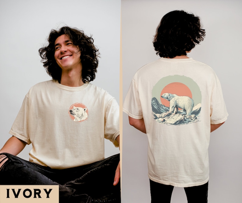 May include: A cream colored t-shirt with a polar bear graphic on the front and a larger polar bear graphic on the back. The back graphic features a polar bear walking on ice with mountains and a sunset in the background. The text "IVORY" is printed in black at the bottom of the image.