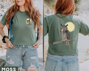 May include: A green t-shirt with a graphic of an owl perched on a branch with a moon in the background. The t-shirt is shown on a person wearing blue jeans.