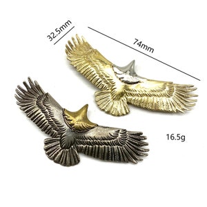 May include: Two metal eagle sculptures, one gold and one silver, with detailed wing and feather designs. The gold eagle measures 7.4 cm wide and 3.2 cm tall, while the silver eagle weighs 16.5 grams.