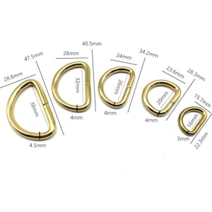 May include: Five gold-colored metal D-rings of different sizes. The rings are measured in millimeters. The smallest ring is 16mm in diameter, and the largest ring is 38mm in diameter.