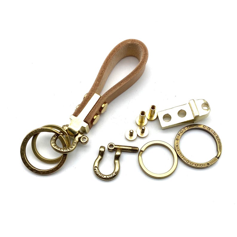 May include: A brass key chain kit with a brown leather strap, two key rings, a hook, a brass plate with the words "Good Luck" and "Good Fortune" engraved on it, and four brass screws.