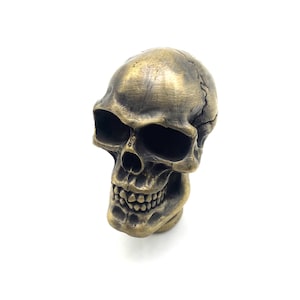 May include: A gold-colored skull figurine with a detailed face and teeth. The skull is made of a smooth, shiny material.
