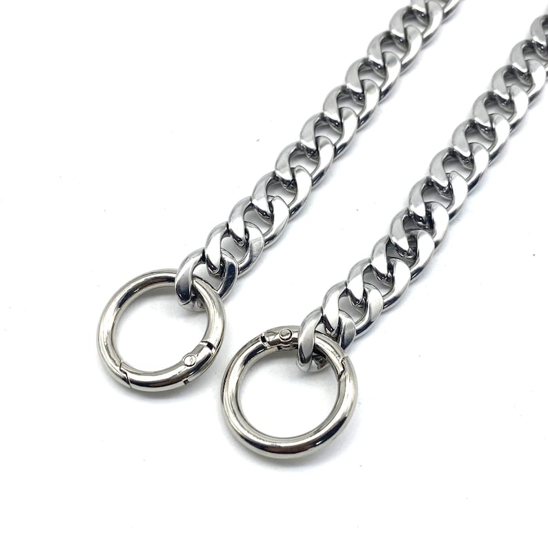 May include: A silver chain with two large, round, silver clasps. The chain is thick and has a curb link design.