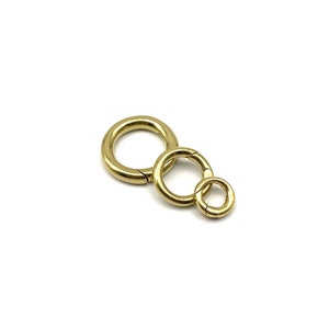 Puede incluir: Tres anillos de metal dorado, cada uno con un diámetro diferente, están unidos entre sí. Los anillos son lisos y tienen un acabado pulido.